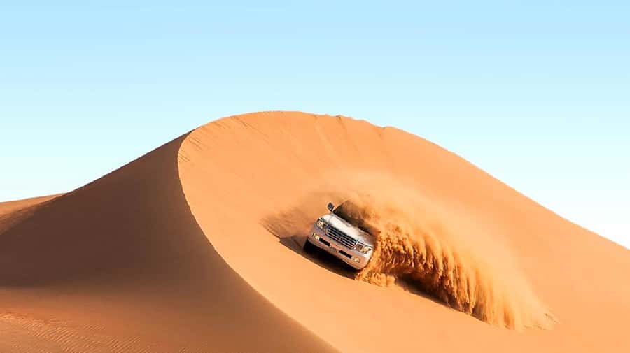 A four-wheel drive cresting a red dune in the Dubai desert